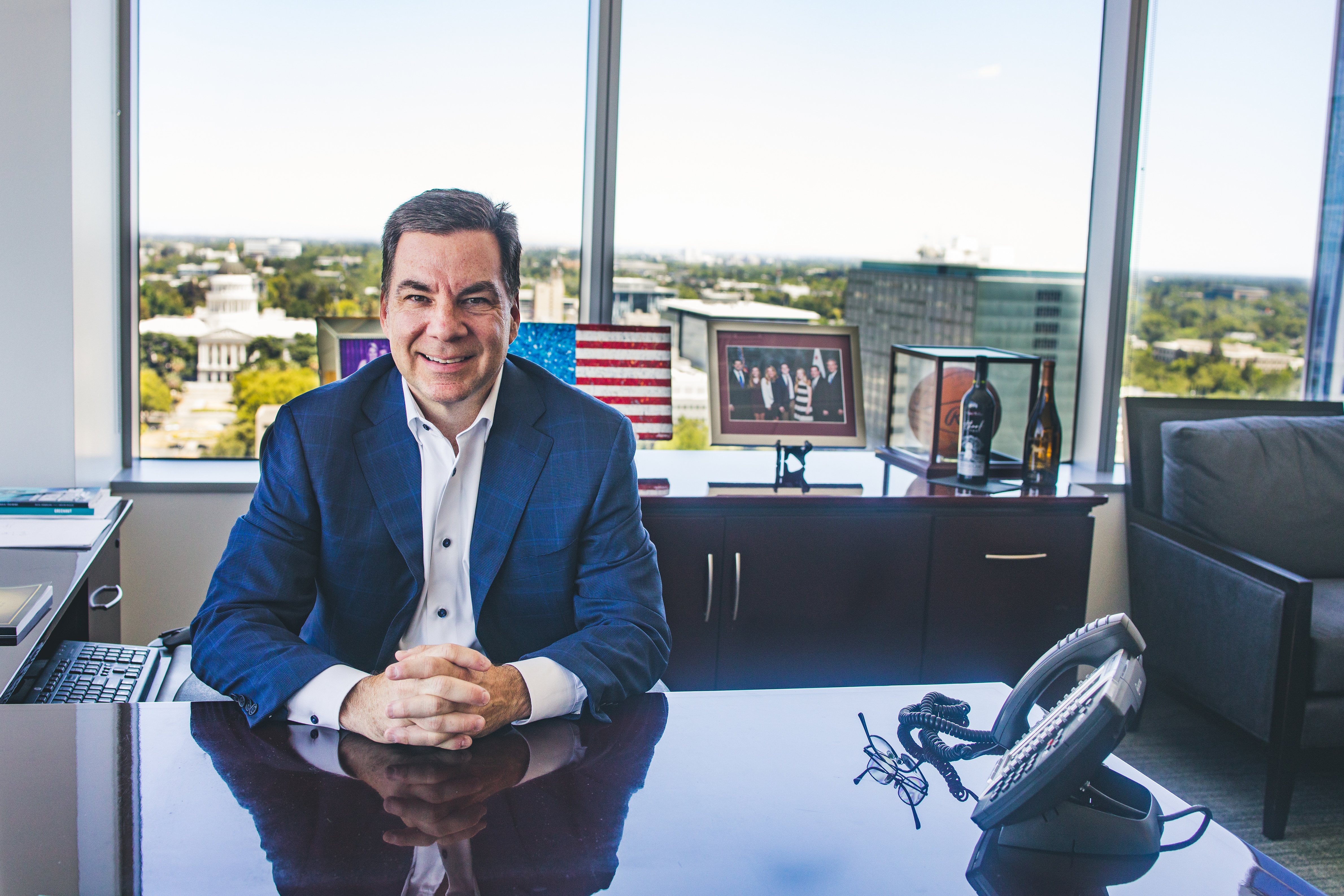 Jeff Randle seated at his desk in his former Capitol Mall office, with Sacramento visible through the windows