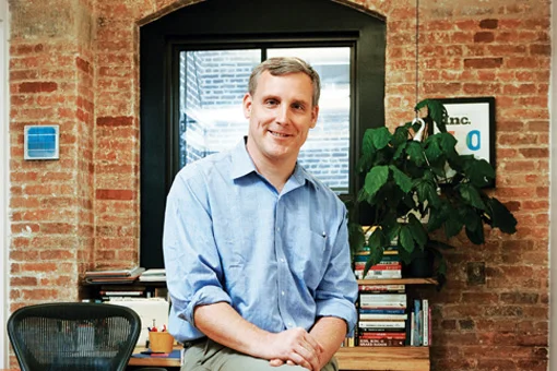 Jeff Stewart sitting on a desk in a brick-walled office