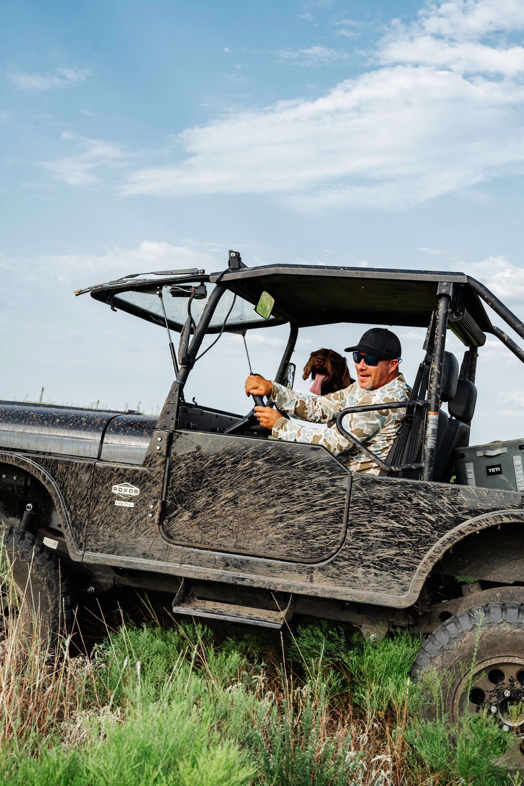 Jeff Tolle drives a mud-marked off-road vehicle with a dog beside him
