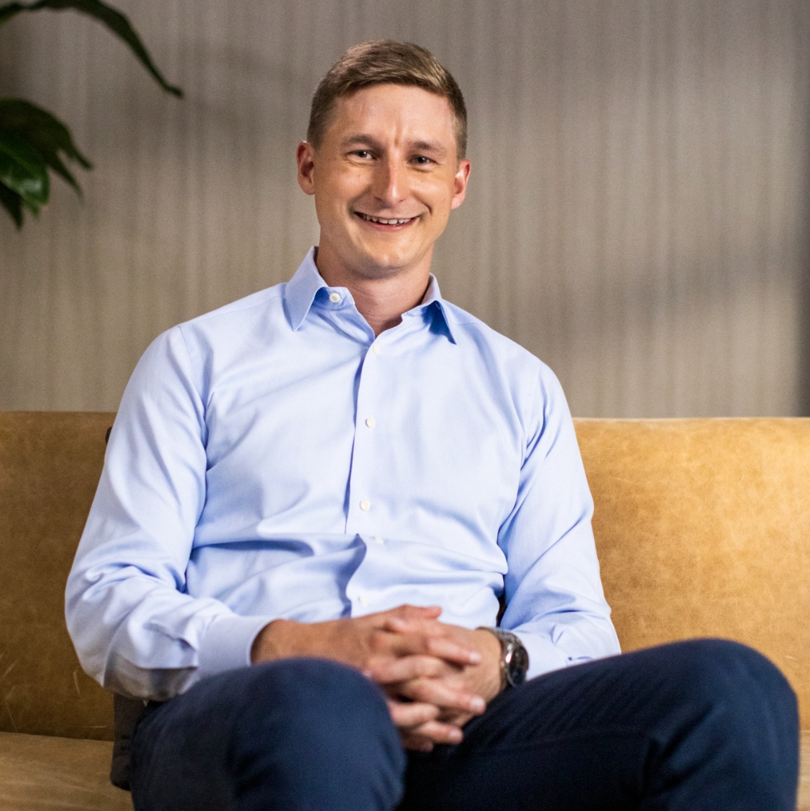 Jeff Totten seated on a mustard-colored sofa, wearing a light blue shirt