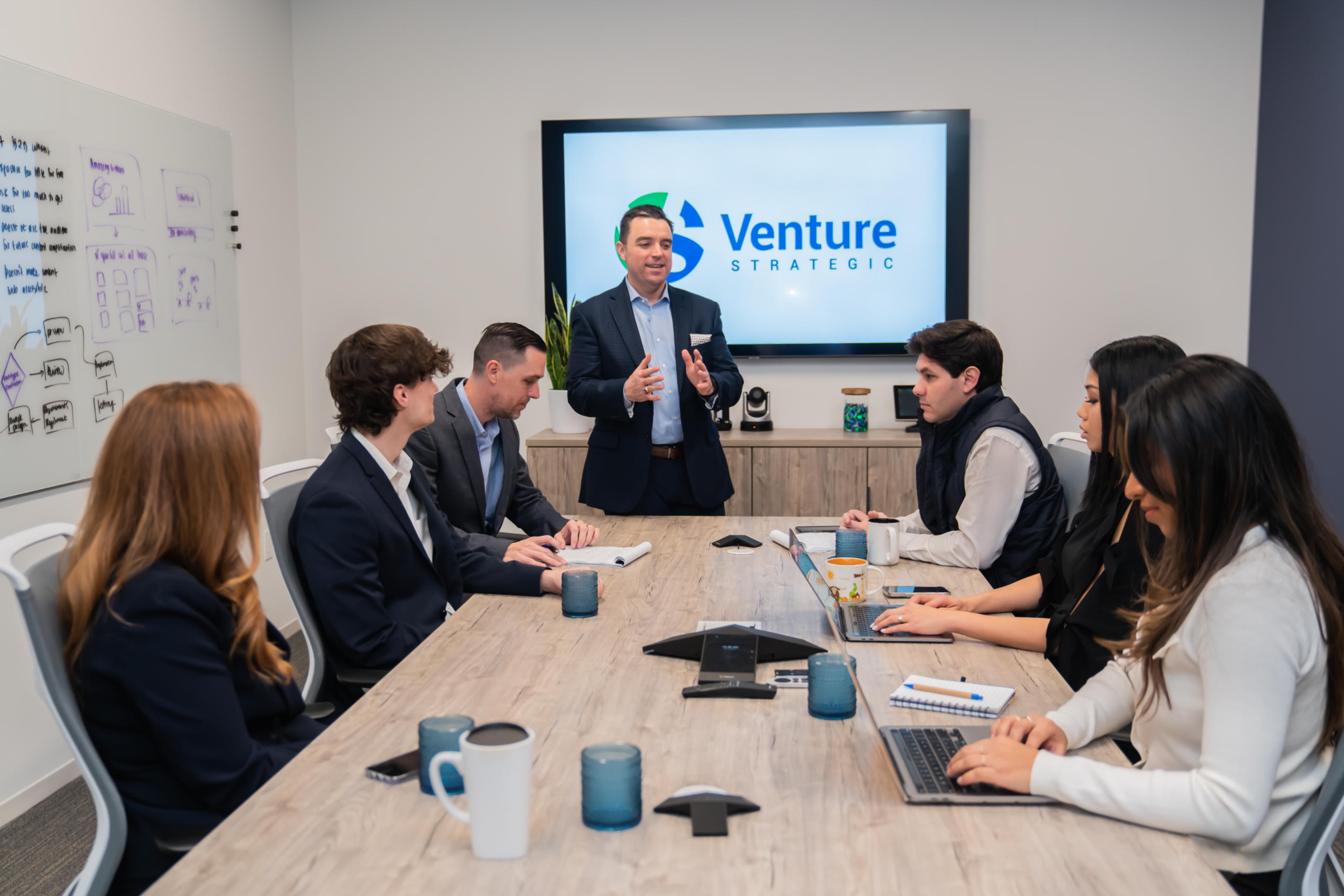 Jeffrey Corless standing at the head of a table during a Venture Strategic team meeting