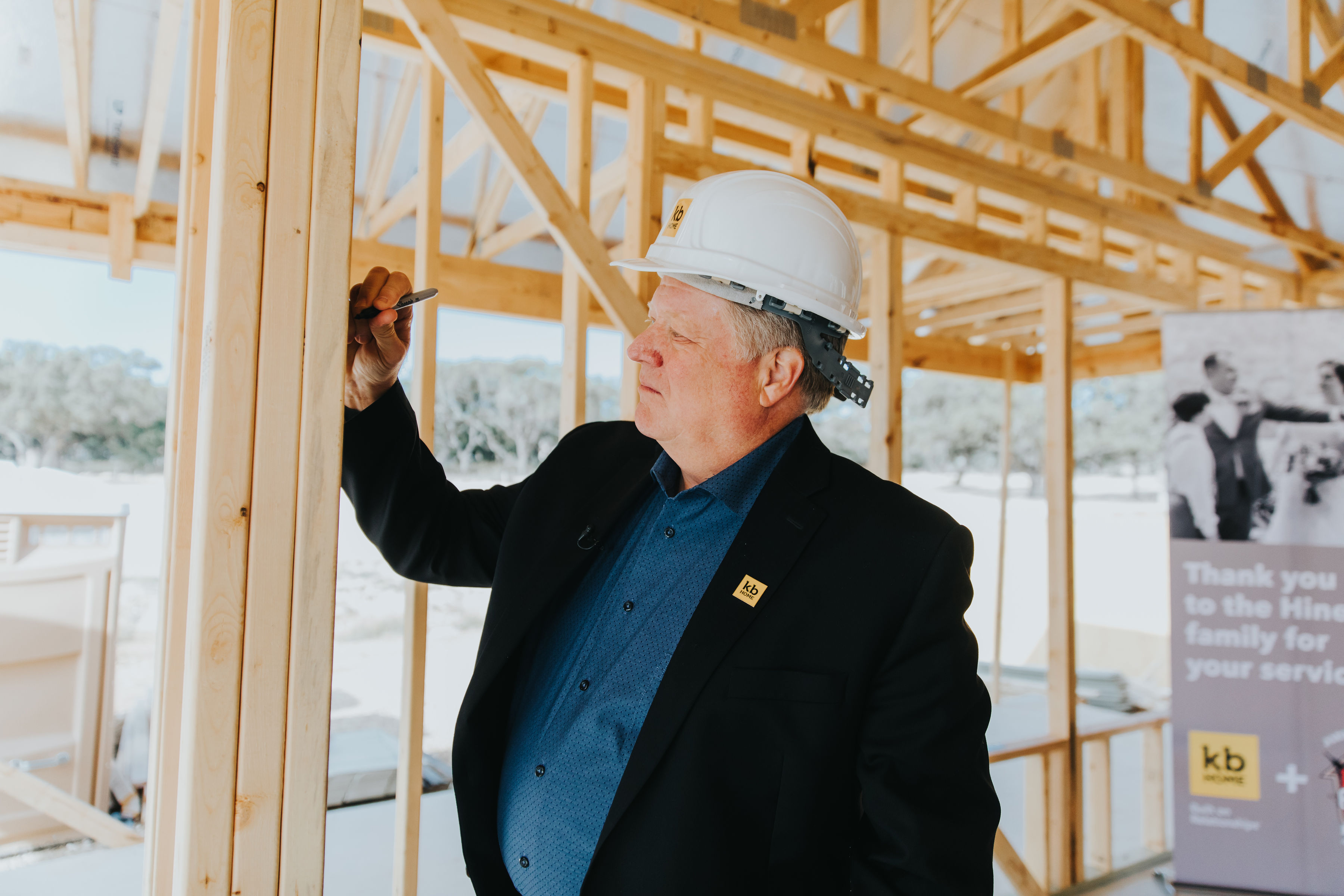 Jeffrey Mezger wearing a hard hat and signing a timber in the frame of a house in December 2019.