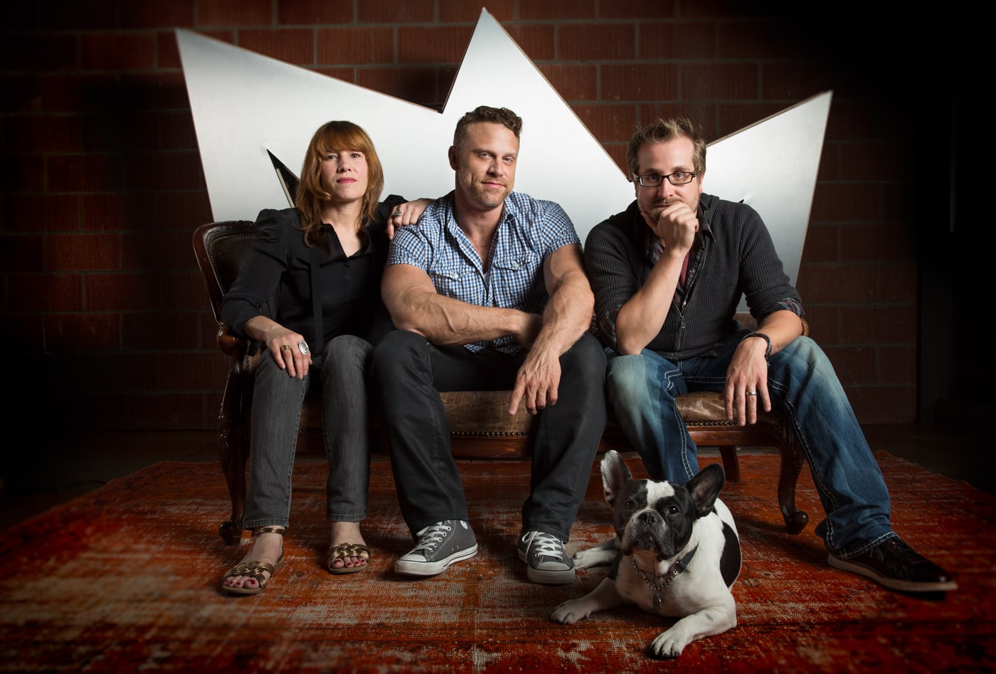 Jen Lucero, Jayson Whitmore and Brien Holman seated together in an archival studio photograph, with a dog in the foreground