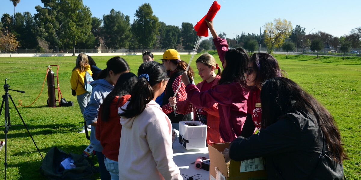 Girls from Project Payload’s 2019 cohort preparing a high-altitude balloon payload outdoors