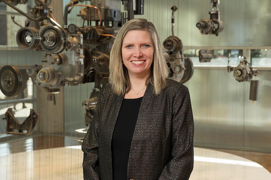Jennifer Rumsey standing in front of a suspended display of engine components