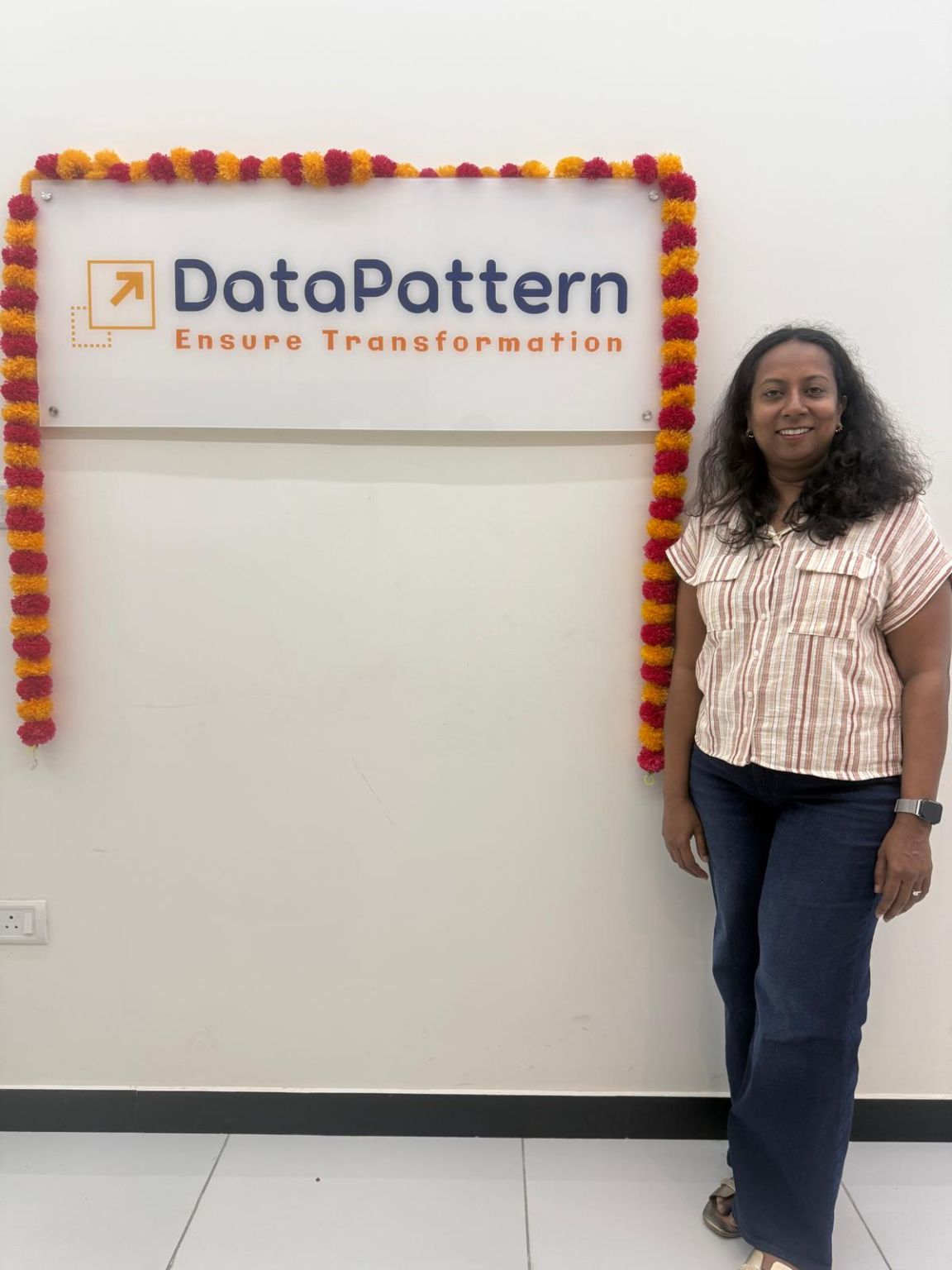 Jennifer Thangam Easwaramurthi standing beside a flower-framed DataPattern office sign