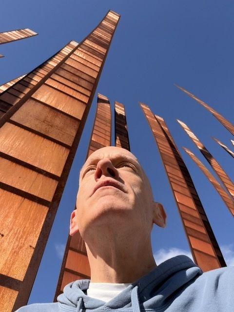 Jensen Harris looking upward beneath copper-colored sculptures and a blue sky