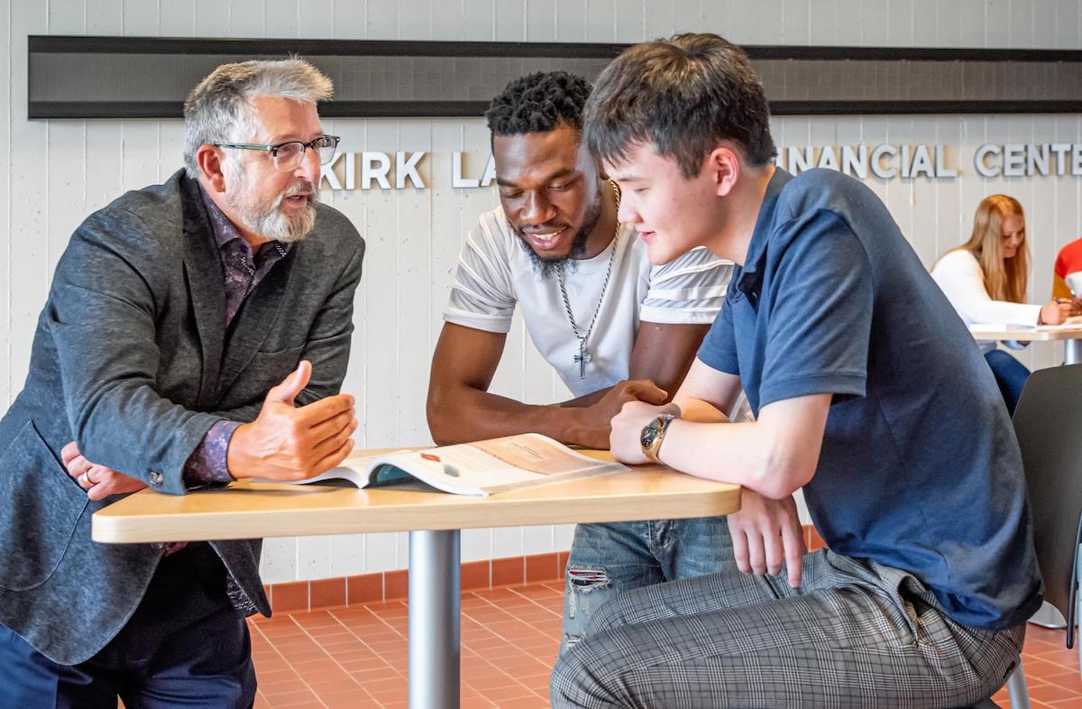 A University of Mary professor talking with two students over an open book