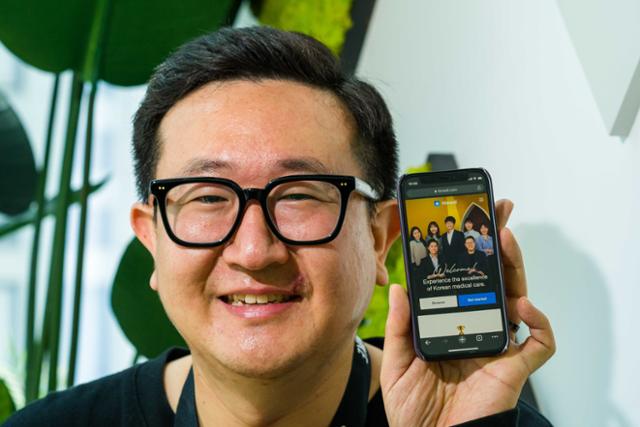 Jeong Ju Lee holding a phone displaying the Himedi platform in his office in 2021