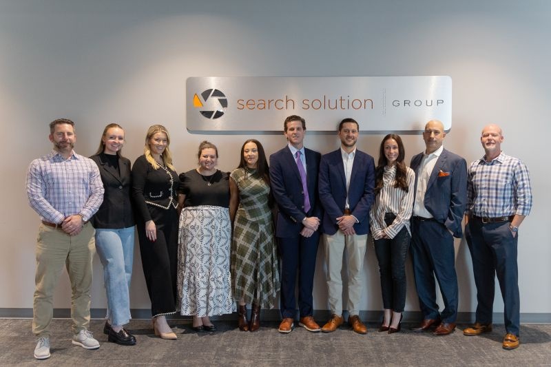 Search Solution Group colleagues gathered beneath the company sign at their 2026 kickoff meeting
