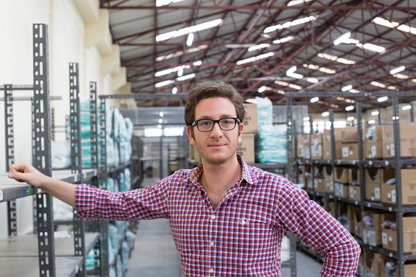 Jeremy Hodara in a checked shirt beside shelves in a Jumia warehouse