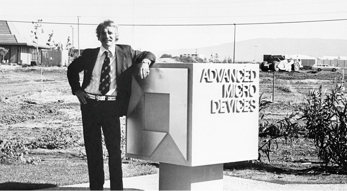 A young Jerry Sanders in a suit, leaning against an Advanced Micro Devices sign beside a developing site