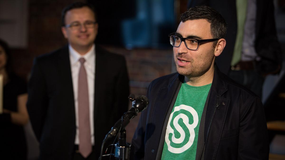 Jesse Lipson speaking at a microphone during a Citrix accelerator event, wearing a green ShareFile shirt and dark jacket