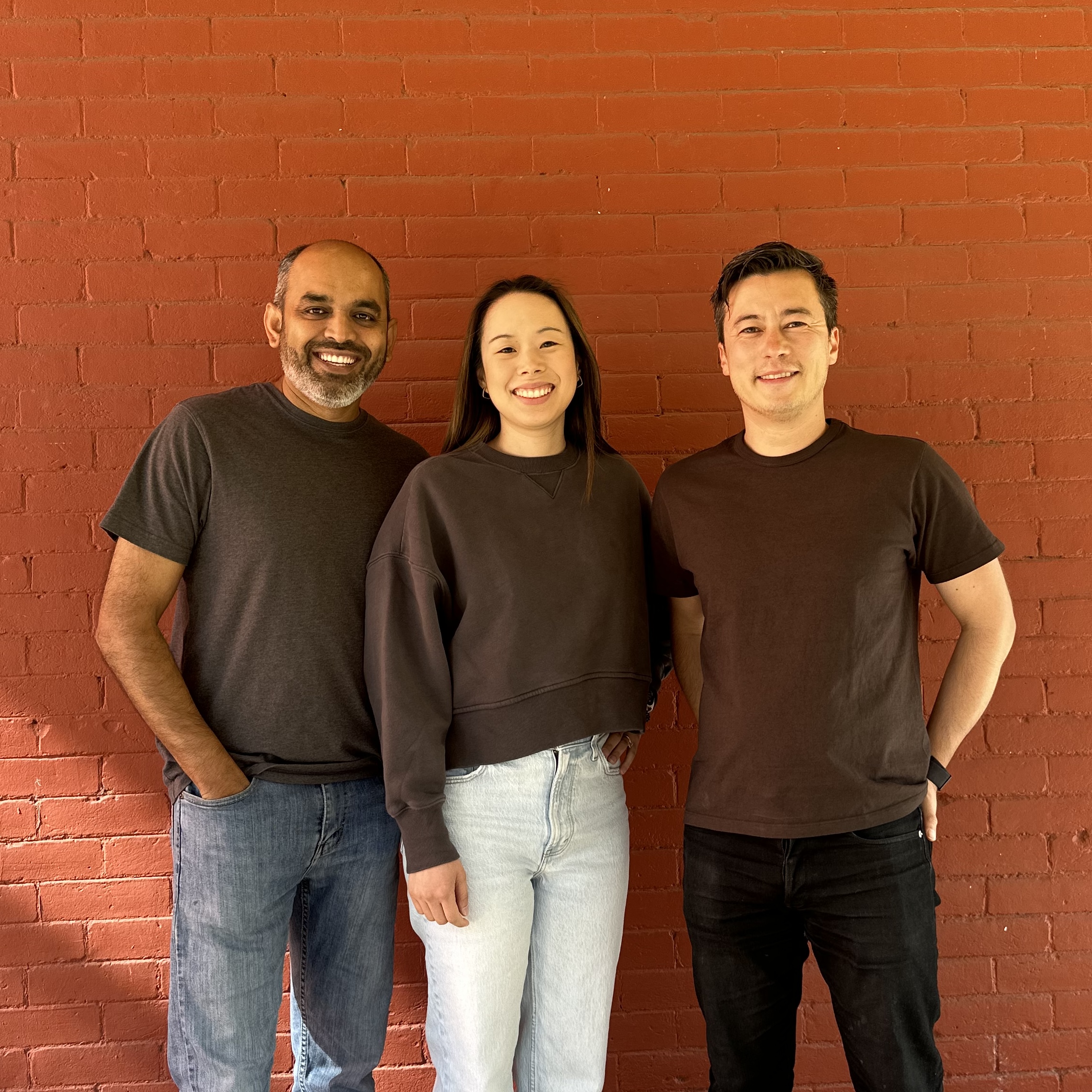 Uprise co-founders Nanthakumar Muthusamy, Jessica Chen Riolfi and Chris Goodmacher standing together against a red brick wall