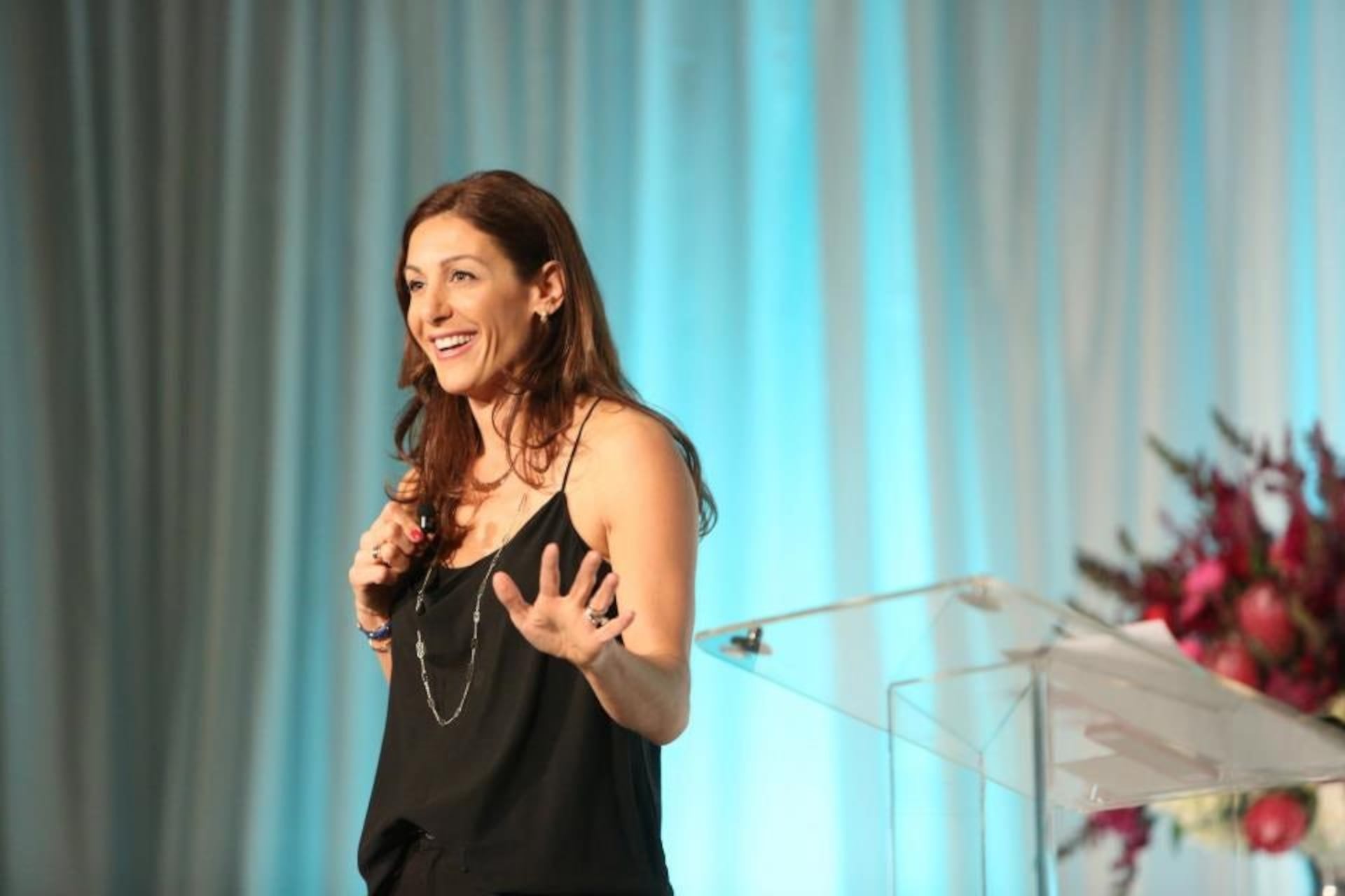 Jessica Herrin speaking into a microphone onstage beside a clear lectern
