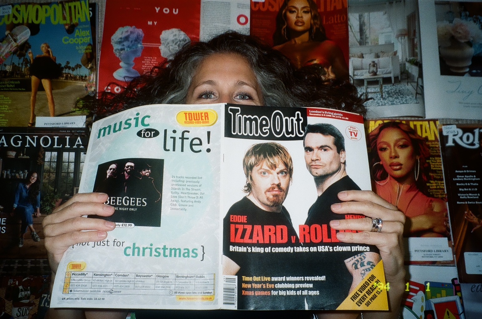 Jessica Savage peeking over an open magazine in front of a wall covered with print imagery