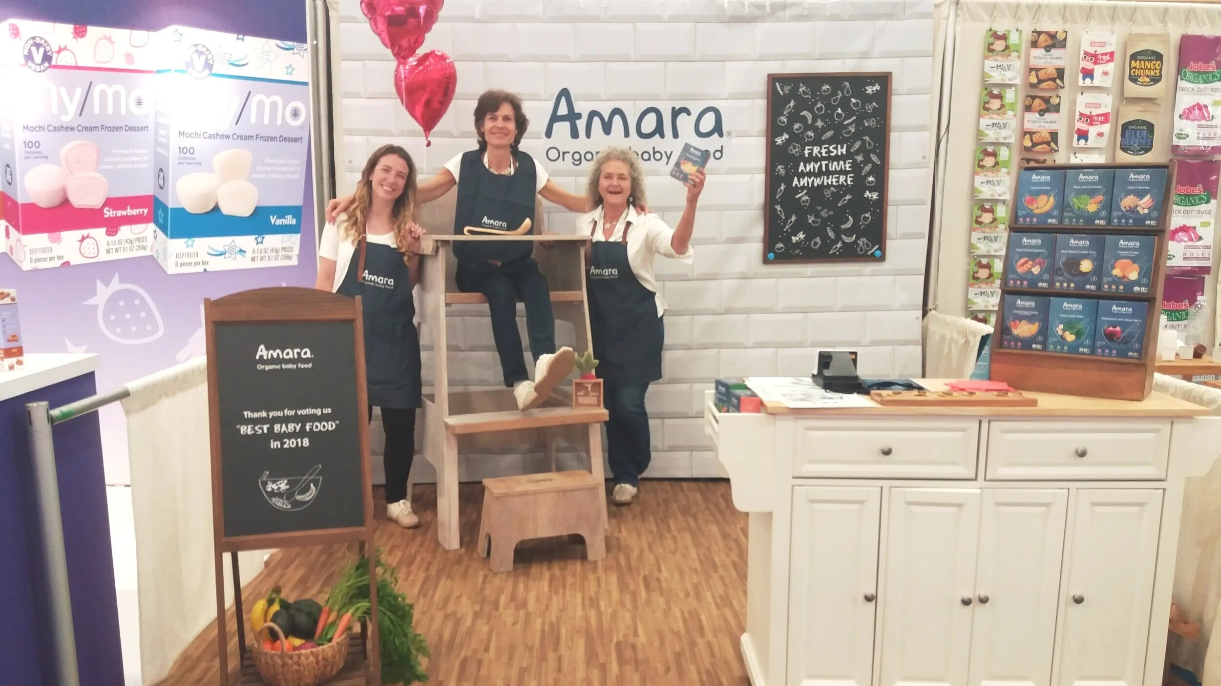 Jessica Sturzenegger, left, with the Amara team beside an oversized wooden high chair at a trade-show booth