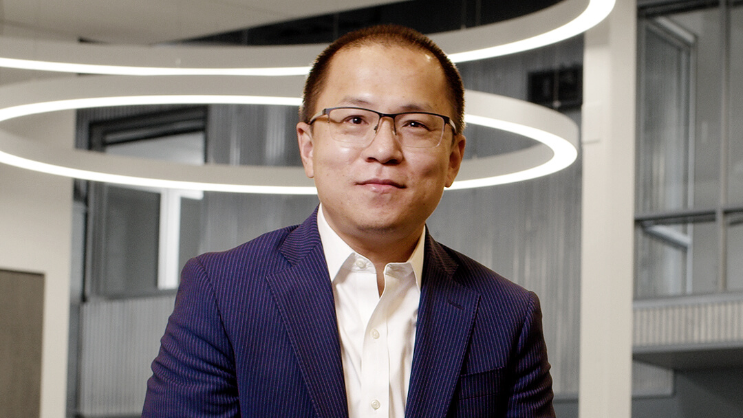 Jian Zhang wearing glasses and a navy jacket in an indoor company press photograph