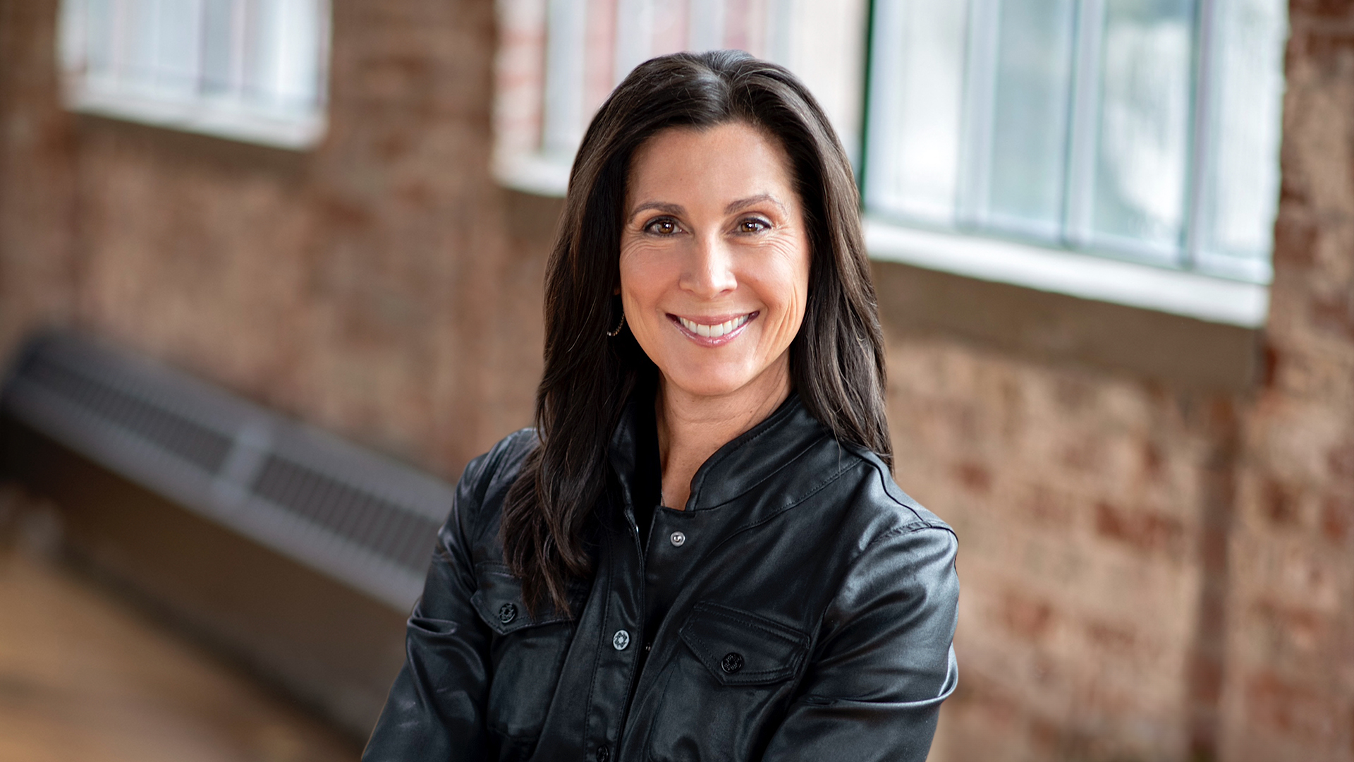Jill Beggs in a black jacket, photographed against brickwork and windows
