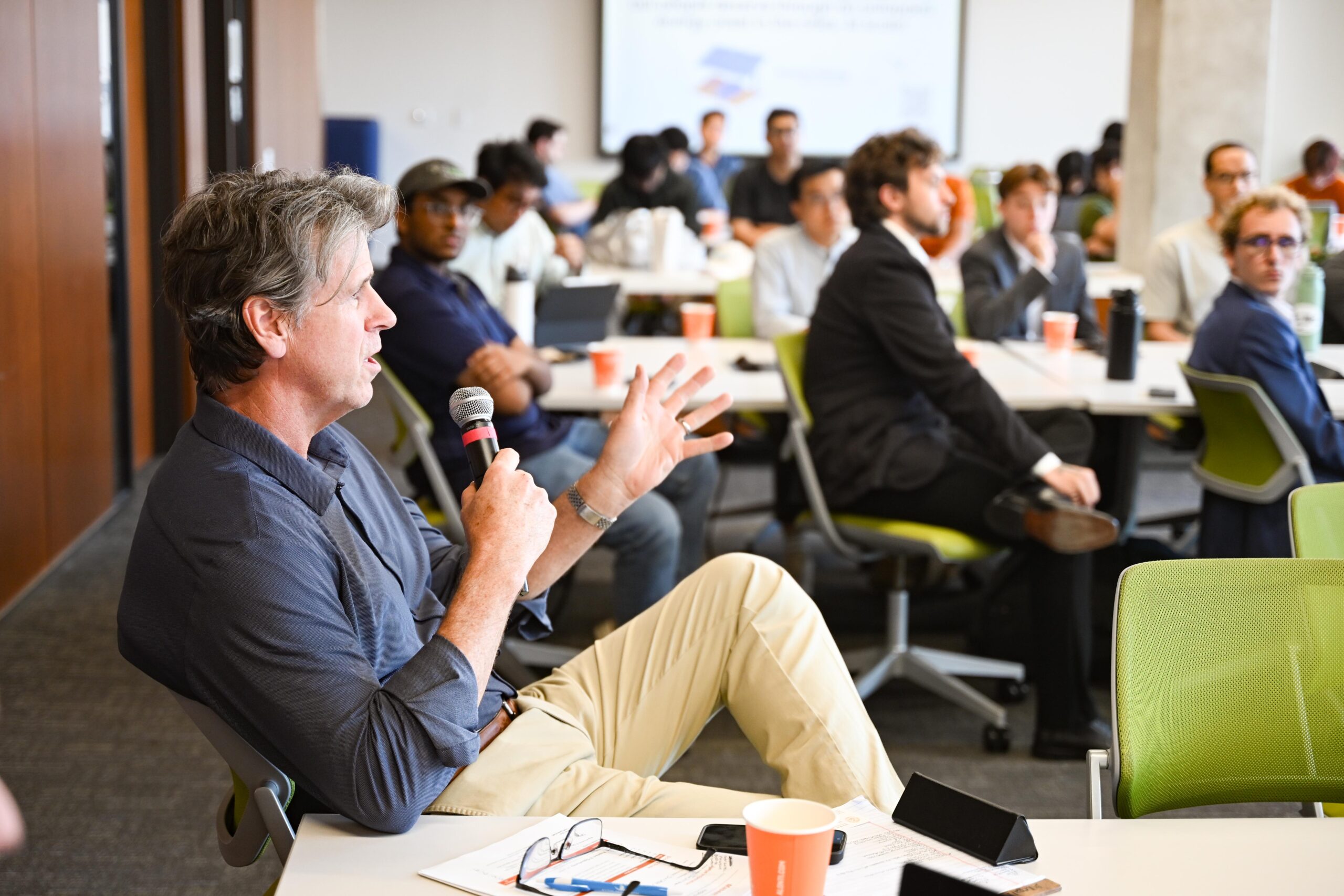 Jim Dechman holding a microphone and giving feedback to student entrepreneurs at UT Austin in March 2026