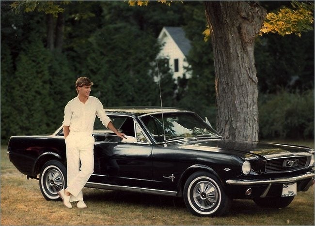 A young Jim Farley standing beside his dark-colored Ford Mustang