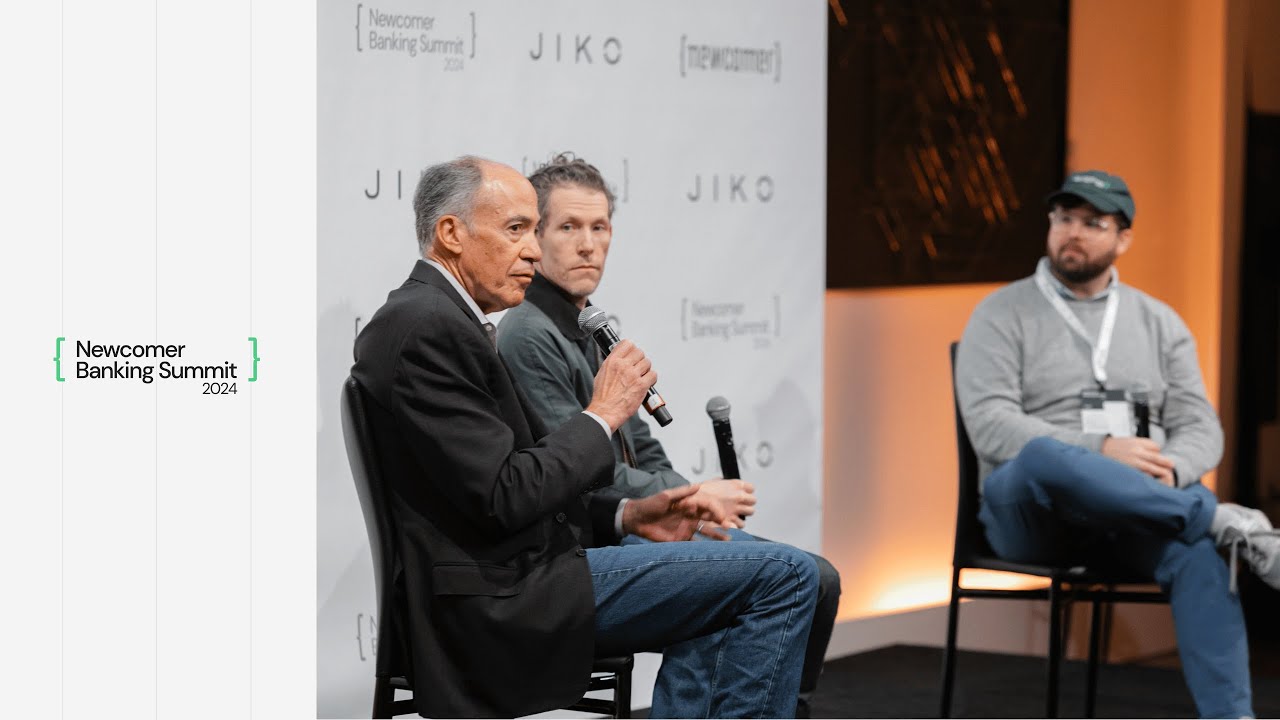 Jim Labe, seated at left with a microphone, speaking on a panel at the 2024 Newcomer Banking Summit.