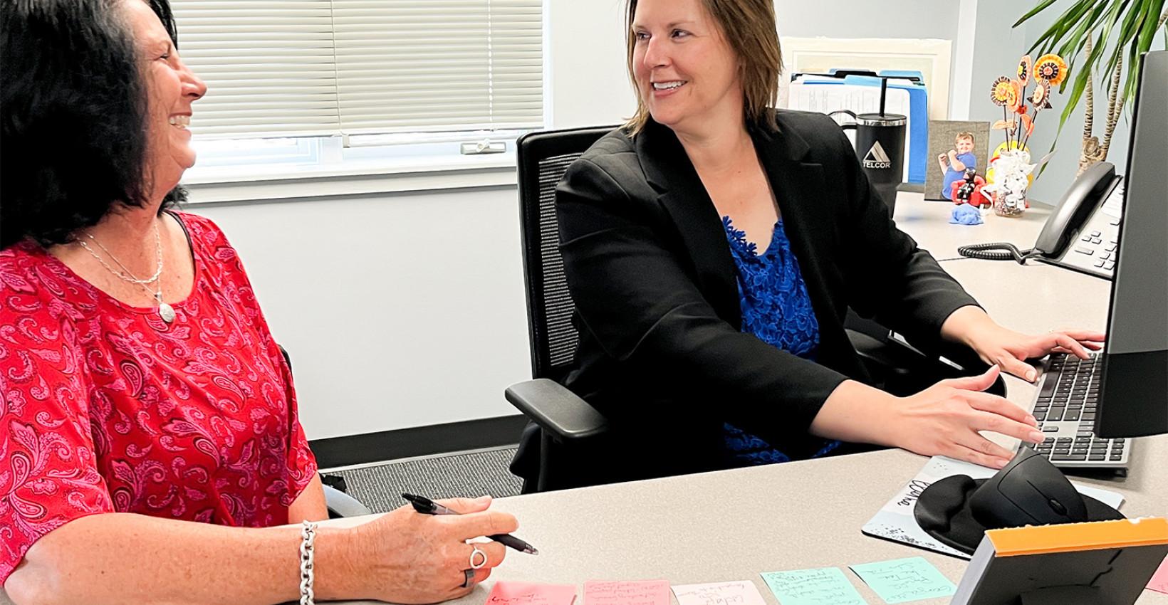 Two colleagues talking at a desk in a TELCOR workplace photograph