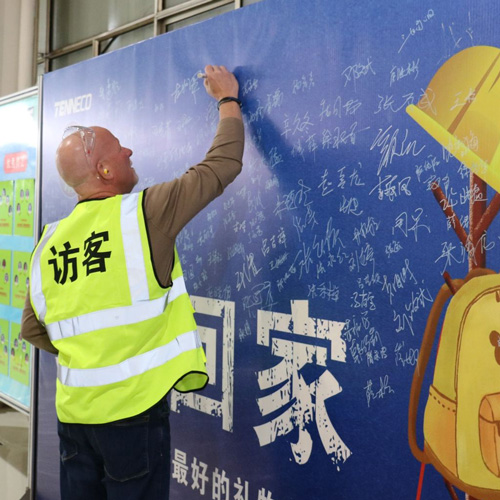Jim Voss wearing a visitor vest and signing a display during a visit in China
