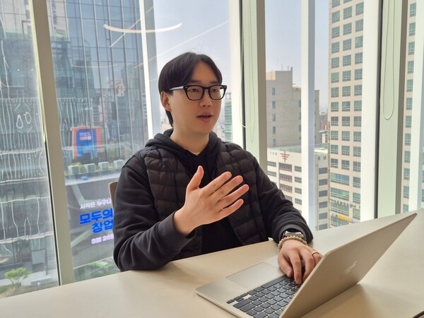Jinu Kim speaking beside an open laptop during an interview