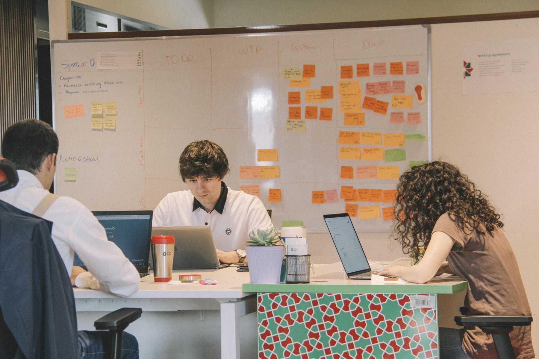Three colleagues working at laptops in front of a wall of agile planning notes