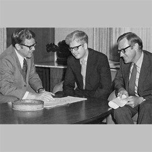 Archival photograph of JJR’s three founding partners gathered around a drawing