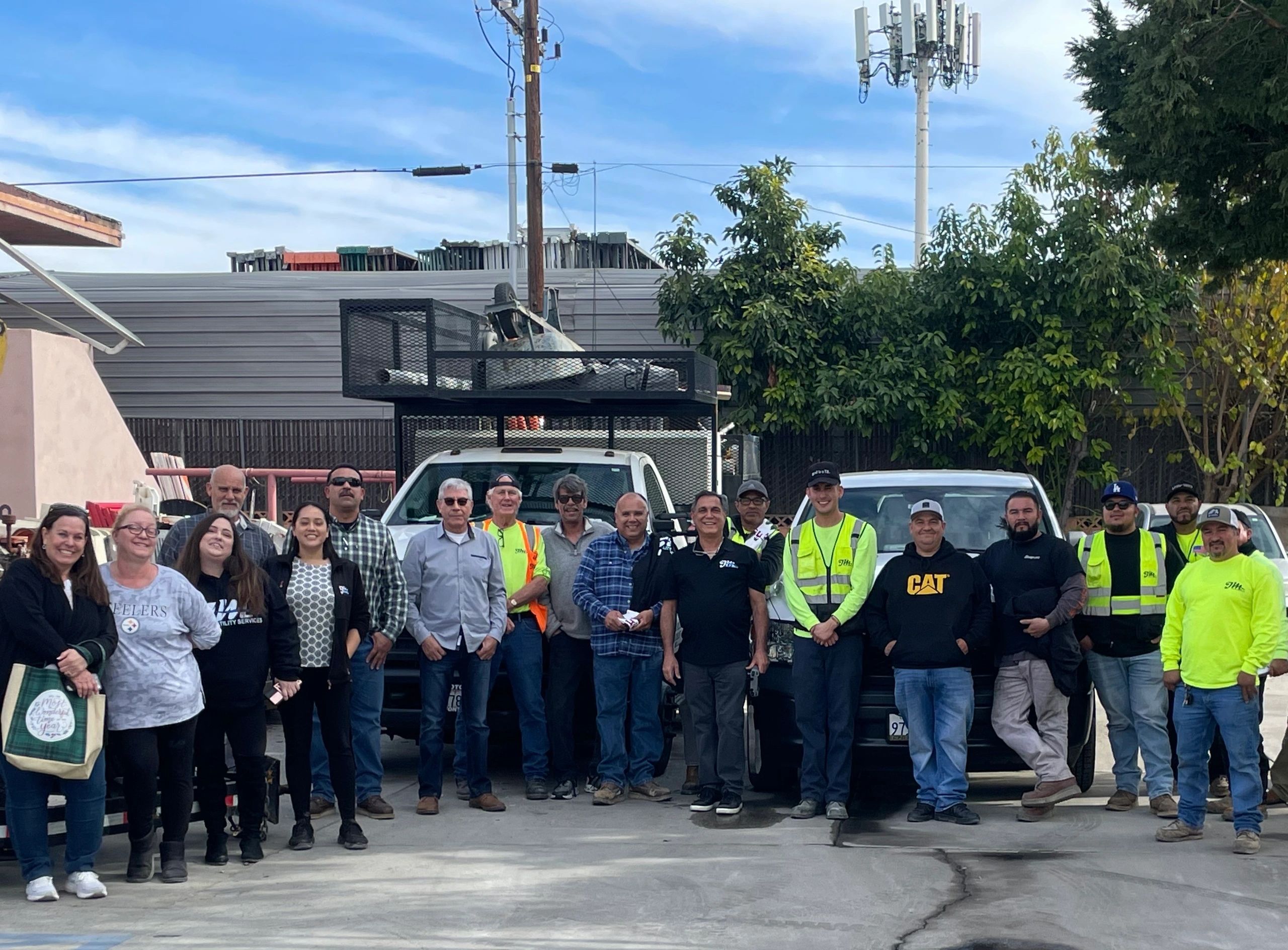 JM Utility Services team standing with work trucks beneath communications equipment