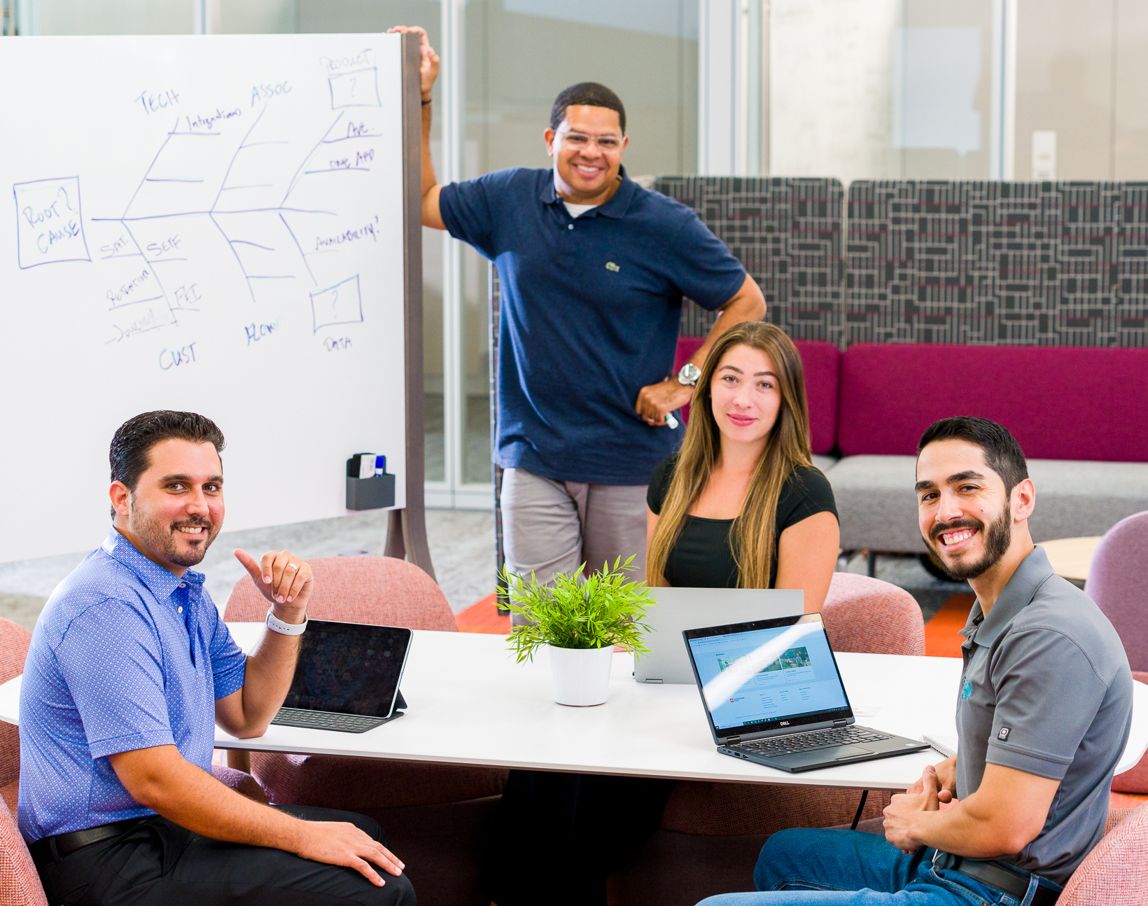Four JM&A associates gathered around laptops and a whiteboard in an office meeting space