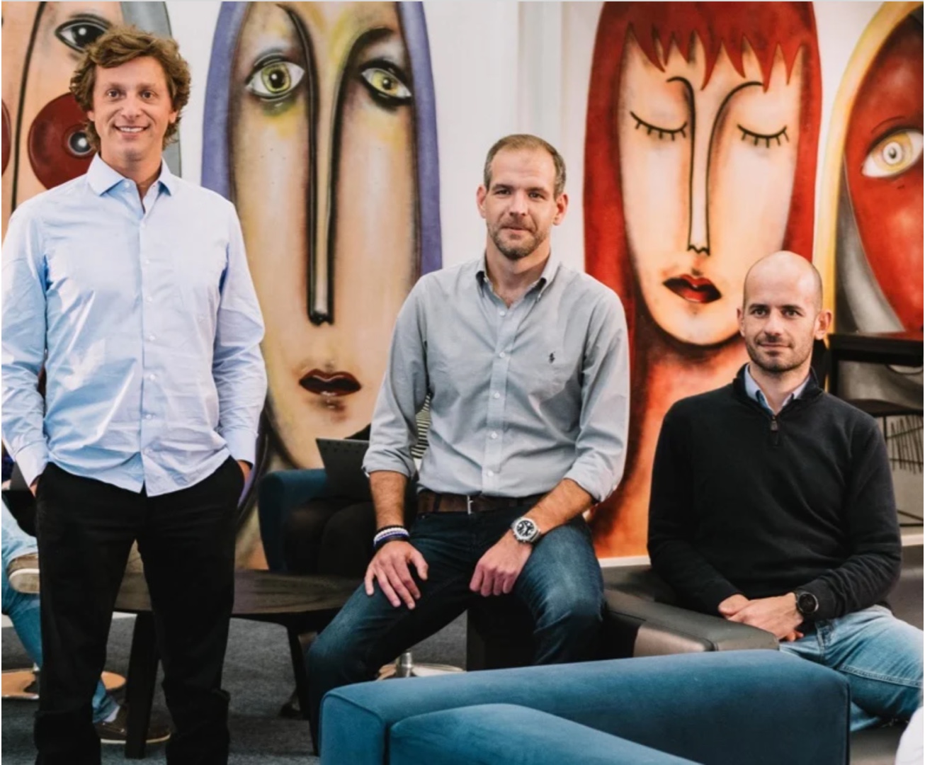 EBANX co-founders Alphonse Voigt standing at left, Wagner Ruiz seated in the centre, and João Del Valle seated at right, in an office lounge.