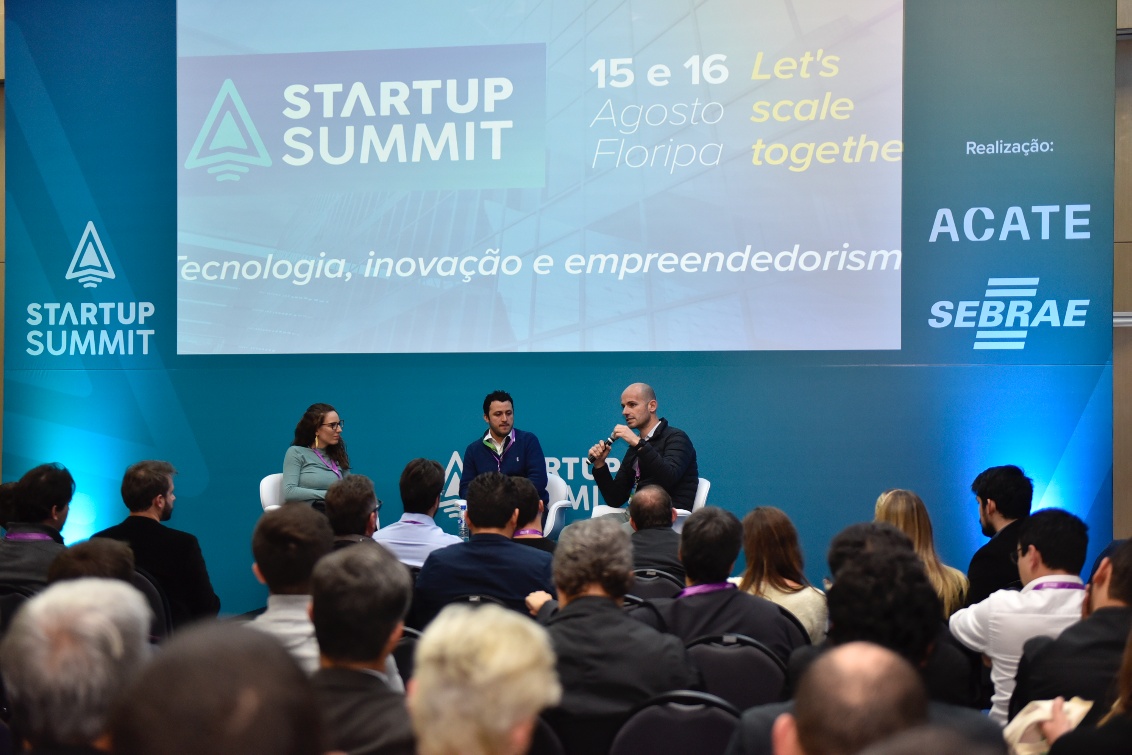 João Del Valle, seated at right with a microphone, speaks on a Startup Summit panel in Florianópolis in 2019.