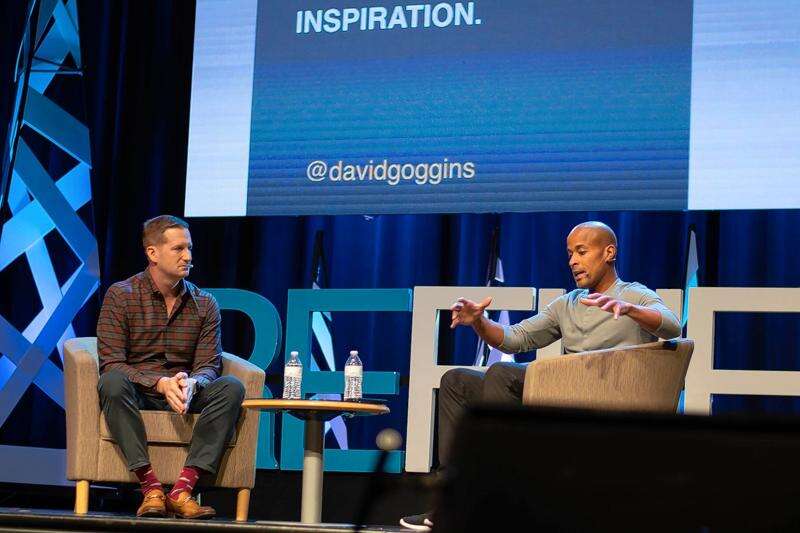 Joe Chura seated at left interviewing David Goggins on stage