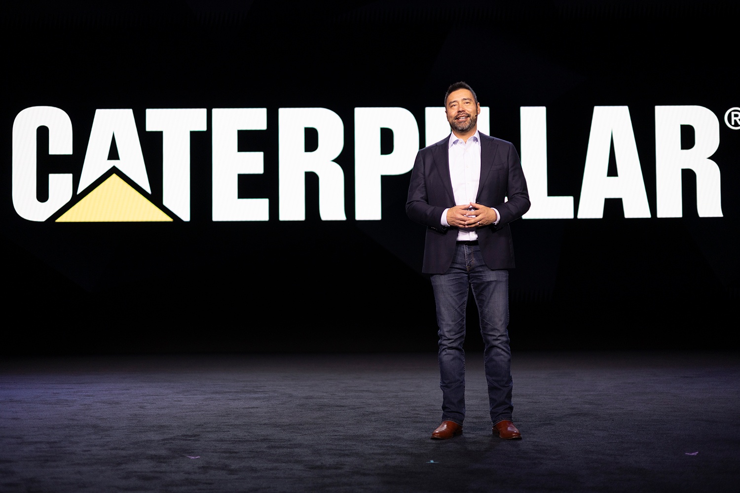 Joe Creed standing on the CES stage in front of a large Caterpillar sign