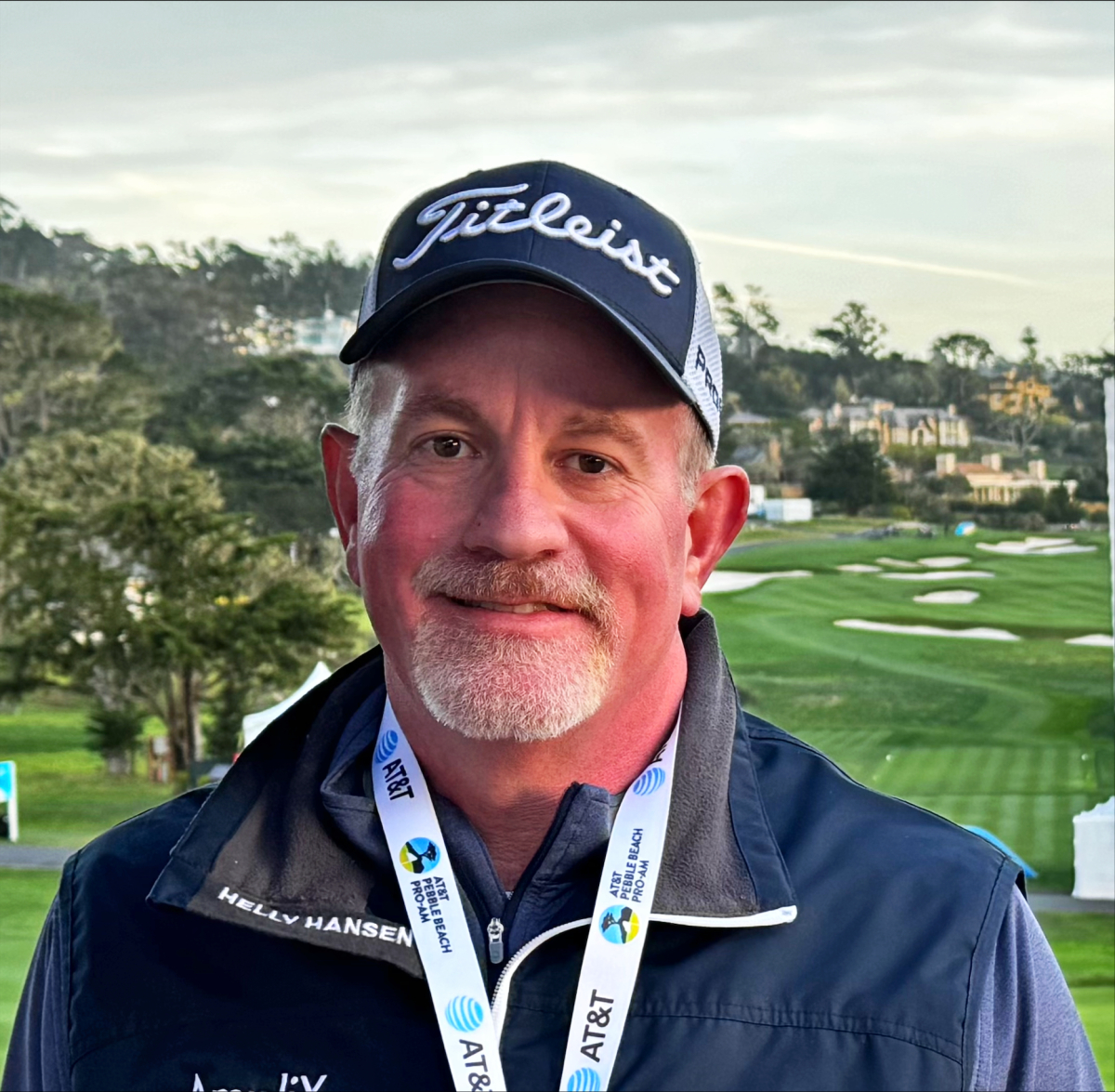 Joe DeStefano in a golf cap and jacket, with a golf course behind him