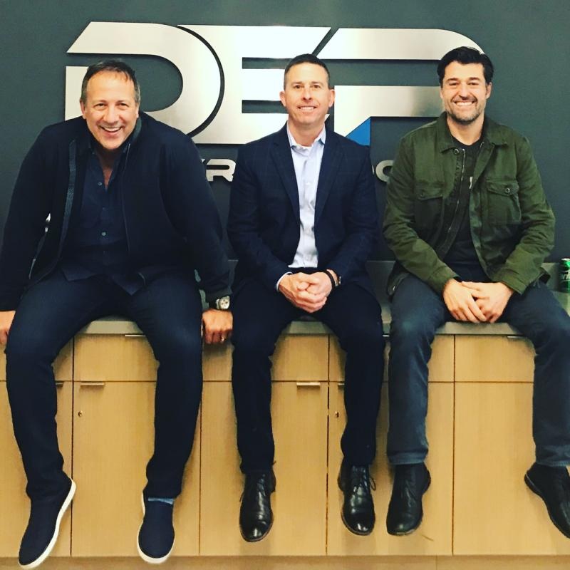 Joe Gillespie, seated at left, with two industry peers in front of Dealer eProcess signage