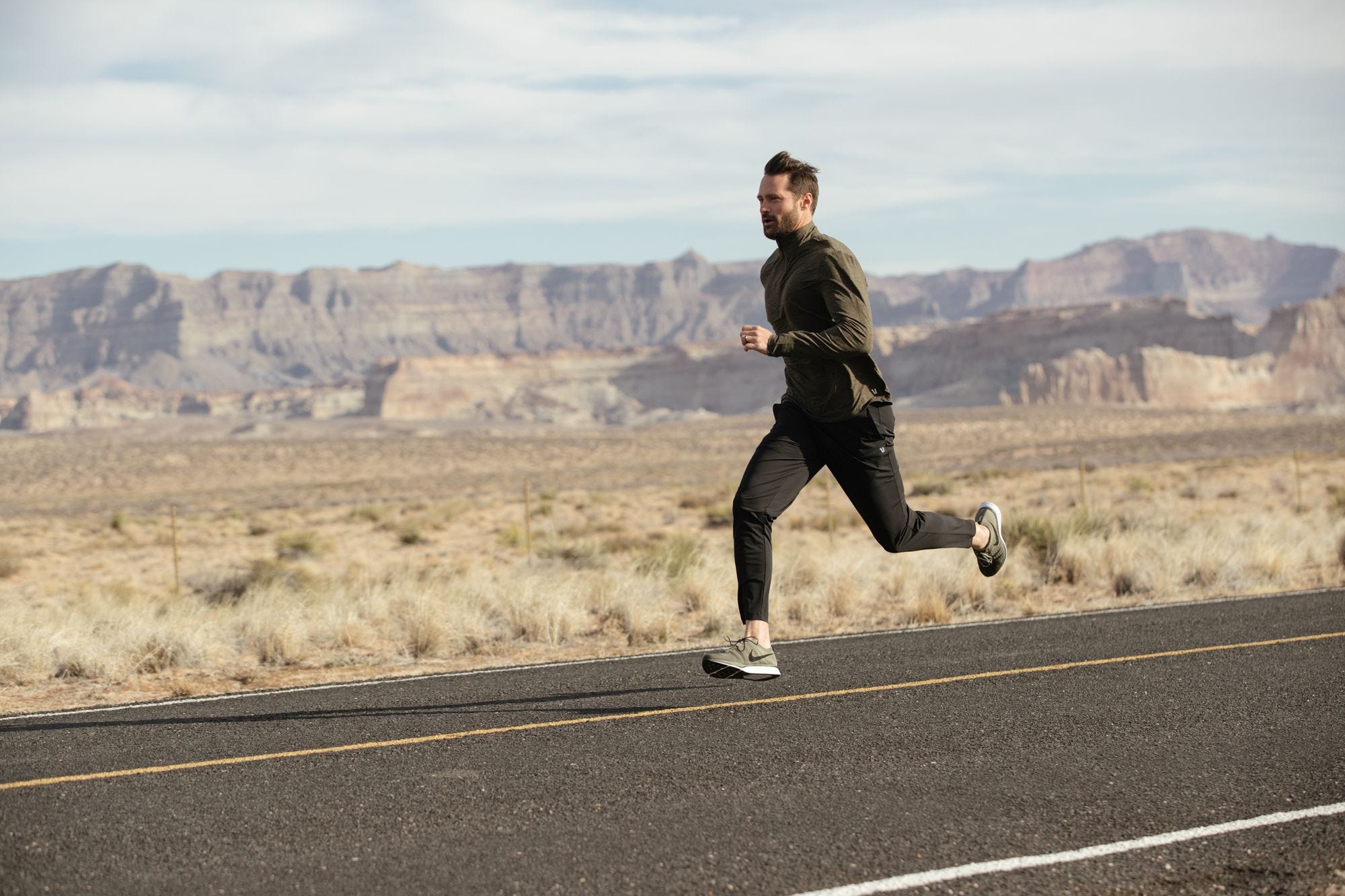 Joe Kudla running along a road with a rocky desert landscape behind him