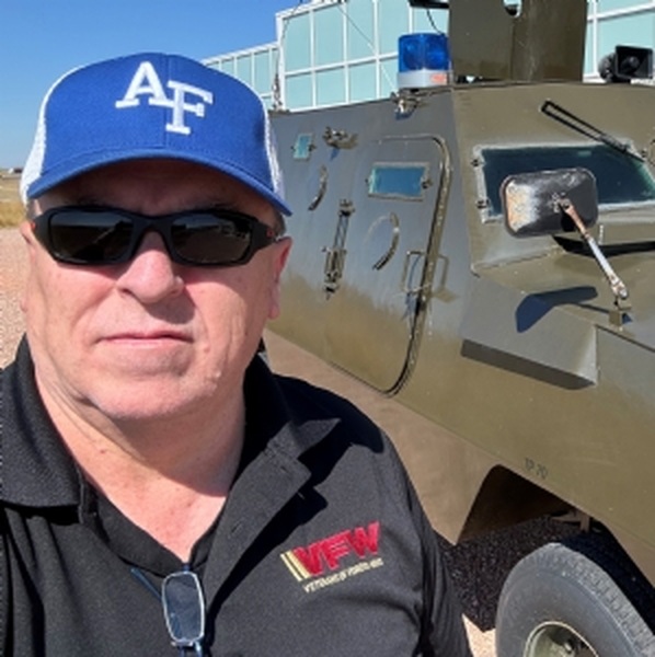 Joe Noplis wearing an Air Force cap beside a military vehicle