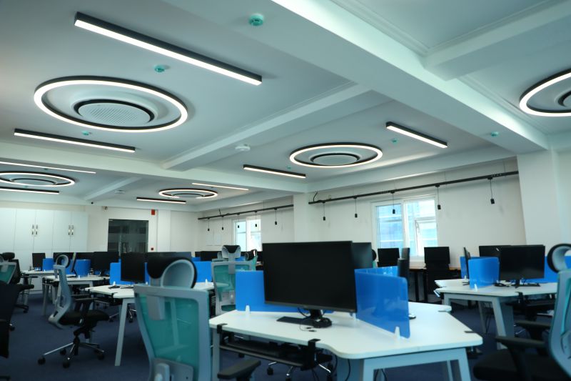 Desks and monitors at Sysvine Park beneath ceiling lights shaped as zeros and ones
