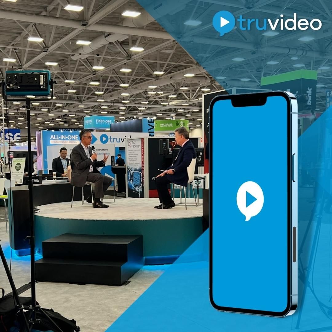 Joe Shaker and Jim Fitzpatrick speaking on a small stage at the NADA trade show beside TruVideo displays.