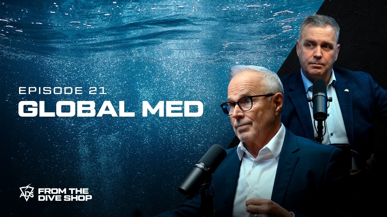 Joel Barthelemy speaking into a microphone during an episode of From the Dive Shop, with GlobalMed executive Sam Price behind him