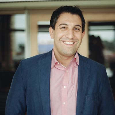 Joel Grossman smiling in a navy jacket and pink shirt