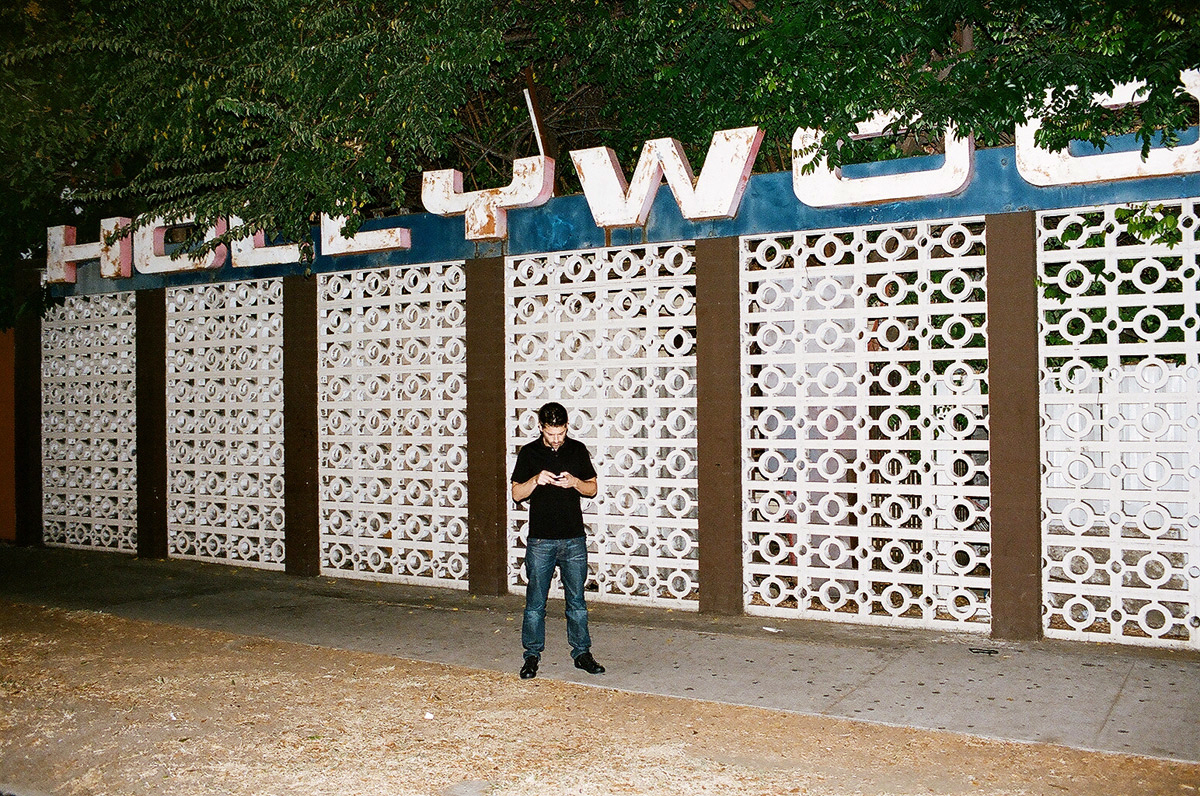 Joel Simkhai looks at his phone outside the Hollywood Center Motel, beneath its large sign and patterned concrete wall