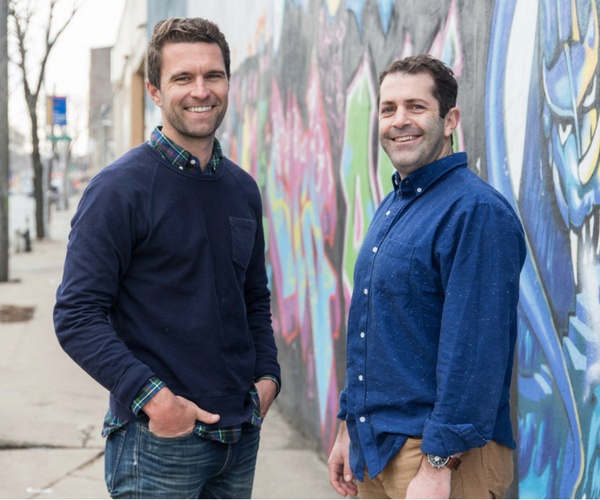 Tim Brown, left, and Joey Zwillinger, right, standing beside a colorful mural