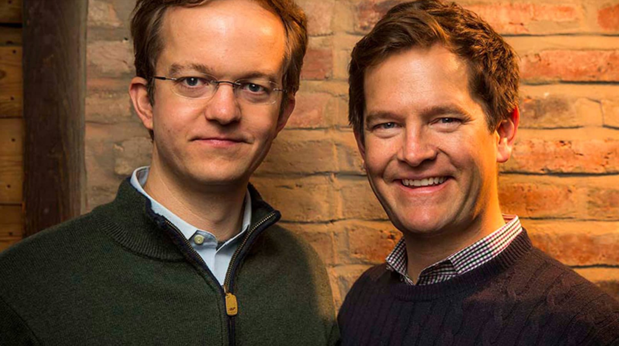 Virtru co-founders Will Ackerly, left, and John Ackerly, right, standing together against a brick wall.