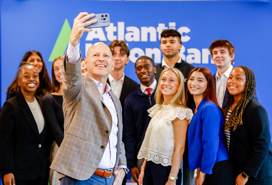 John Asbury holding up a phone for a group selfie with young adults in front of an Atlantic Union Bank backdrop