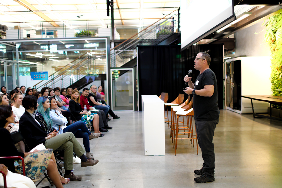 John Beatty holding a microphone while speaking to an audience at Clover’s Sunnyvale office